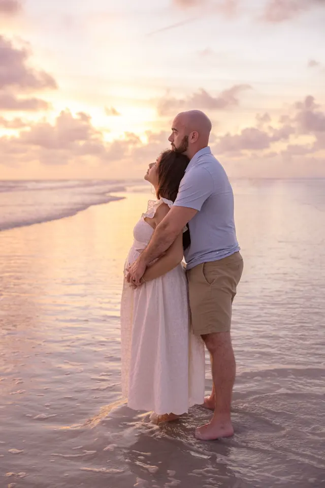 Expecting couple standing in the water at sunset